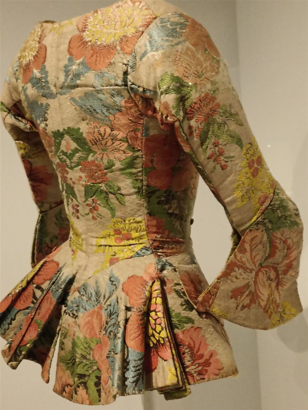 Jubón de seda del siglo XVIII tejido en espolín, con flores de colores, en un museo